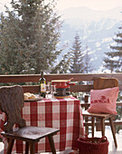 Stühle und Tisch mit kariertem Tischtuch auf einem Balkon mit Bergblick