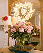Arrangement of pink roses in glass vase on table in front of mirror