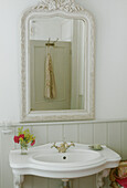 Mirror above old fashioned wall mounted washbasin in country style bathroom
