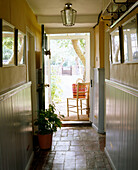 A country yellow hallway tiled floor part wood panelling open front door to garden lamp wooden chair