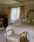 Ein traditionelles Schlafzimmer mit Balkendecke, Doppelbett, Vorhängen und einem verschnörkelten Empire-Hocker