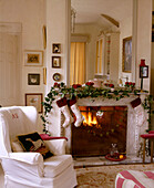 A traditional sitting room containing a mirror above a large open fire with Christmas stockings and decoration hanging from the mantelpiece