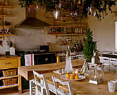 A traditional kitchen with decorations suspended above a large wooden kitchen table and an extractor fan above an stove