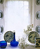 Display of blue glass bottle and china pieces on window sill