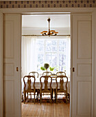 View through open door to traditionally Swedish dining room with dining table and Gustavian chairs
