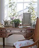 A detail of a traditional bedroom wooden dressing table with a silver framed mirror and potted plants on top