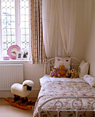 A traditional young girls bedroom with a rocking sheep and teddy bears on the bed
