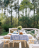 Garden table covered with a tablecloth with wooden benches either side on a decked area with a white fence