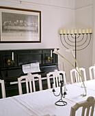 The view looking across the dining table towards a framed print above a piano next to a large candelabra