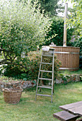 A rustic wooden step ladder in the garden next to a wicker basket and a fruit tree