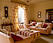 Two sofas and patterned curtains in living room with striped ottoman