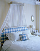 Swedish style bedroom with blue and white checked upholstered headboard and canopy on bed