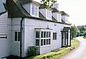 An exterior view of a white washed stone cottage front door porch attic windows in a rural setting