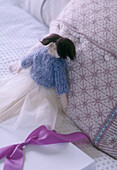 A detail of a bedroom bed with a doll figure a knitted cushion