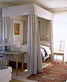 White wood Gustavian chair next to four poster bed with drapes