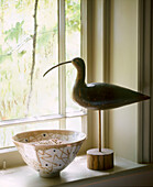 Detail eines Fensters im Landhausstil mit einer Keramikschale und einem hölzernen Vogelköder auf der Fensterbank