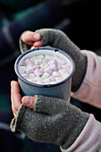 Mädchen mit Marshmallow-Getränk in fingerlosen Handschuhen, Wiltshire, UK