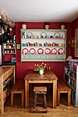 Wall mounted cabinet with wooden bench seats and table in red kitchen of Bridport home, Dorset, UK