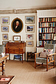 Framed pictures and bookcase with antique bureau and upholstered chair in 17th century Hampshire home, UK