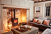 Candlelit inglenook fireplace with sofa and ottoman in Grade II listed farmhouse Kent, UK