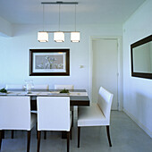 Dark oak dining table with white leather chairs below aluminium and frosted glass ceiling light