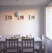 Tisch, sechs Holzstühle, eine moderne Leuchte und drei gerahmte Kunstwerke an der Wand mit Obstapplikationen