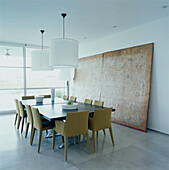Zeitgenössisches, minimalistisches Esszimmer mit Esstisch, Stühlen, einem großen Bild, Steinböden und einer glasgetäfelten Wand