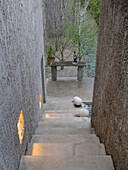 Blick über eine Treppe hinunter zum Garten im Zen-Stil mit strukturierten Betonwänden und Kies