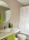 Badezimmer mit gepunktetem Duschvorhang und rundem Spiegel