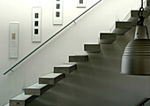 Floating staircase with concrete cement steps and handrail with artwork and metal pendant lamp