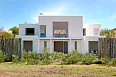 Weiß verputzte Außenwände eines Hauses mit Akazien-Eukalyptus-Blockzaun