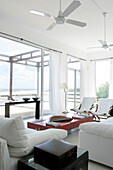 Huge windows overlooking the sea with linen curtains and a Chinese wood table lacquered in red with golden motifs sofas and deck-chairs in white canvas