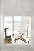 Huge windows overlooking the sea with linen curtains and a Chinese wood table lacquered in red with golden motifs sofas and deck-chairs in white canvas