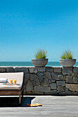 Beach house exterior with plant pots on stone wall with sun lounger