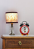 Child's alarm clock and lit lamp on chest of drawers