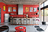 Recycled kitchen counter with Lapacho top and cast iron stools with black leather seats with plastered walls painted red