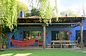 Blau gestrichene Veranda mit Markise aus Naturholz und kontrastierender roter Hängematte