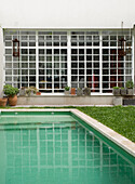 Large white window facing onto swimming pool set in lawned garden