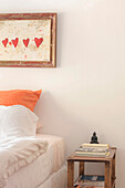 Bedroom detail with bright orange pillow beneath heart shaped artwork