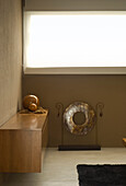 Wooden sideboard and metal gong below closed roller blinds