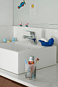 Toothbrushes and toothpaste beside ceramic wash basin with soap dish and tap