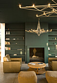 Green fireplace and bookshelves with mustard coloured leather armchair and modern light fitting