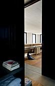 Bücher auf Regal in schwarzem Interieur mit Blick durch Türöffnung auf Stuhl an leerem hölzernem Frisiertisch