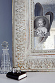Ecke des geschnitzten Bilderrahmens mit Glaskaraffe und schwarz-weißem Porträtbild