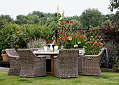 Cane furniture at garden table with flowers in bloom