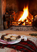 Mince pies and pinecones on tartan blanket next to open fire