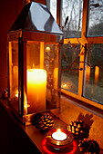 Lit candle on Victorian schoolhouse window with pinecones