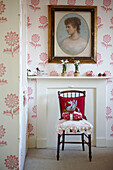 Wooden chair under portrait in bedroom with floral patterned wallpaper