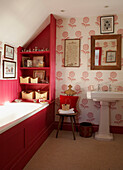 Panelled red bath in floral wallpapered bathroom with freestanding wash basin