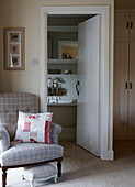 Grey upholstered armchair in bedroom with panelled door opening to ensuite bathroom
